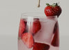 A glass of strawberries and pink water being stirred